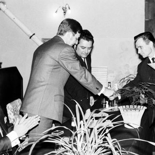 Three men in suits standing near a table with plants.
