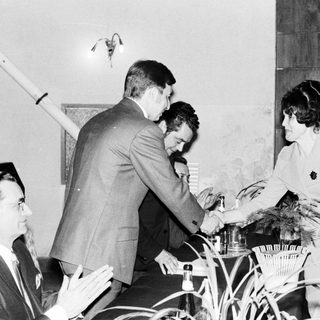 Man receives an award from a woman, onlookers applaud.