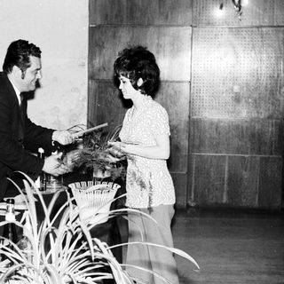 Man presenting a certificate to a woman, onlookers present.