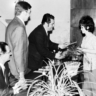 Man presenting a certificate to a woman, onlookers present.
