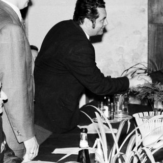 Men in suits shake hands near a table with plants.