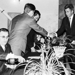 John F. Kennedy shakes hands with someone at a table.