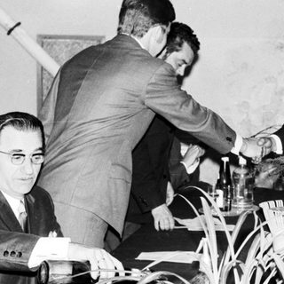 John F. Kennedy shakes hands with someone at a table.