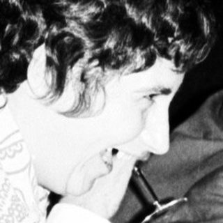 Woman in patterned dress leans over a table, men nearby.