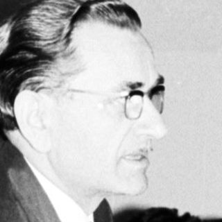 Man in suit stands near a table with people.
