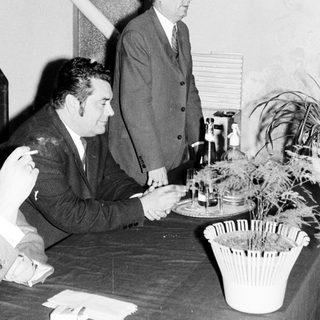 Men seated at a table, with one standing nearby.