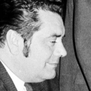 Men seated at a table, with one standing nearby.