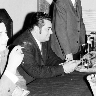 Men seated at a table, with one standing nearby.