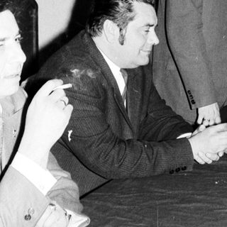 Men seated at a table, with one standing nearby.