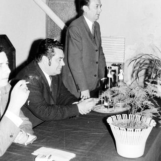 Men seated at a table, with one standing nearby.