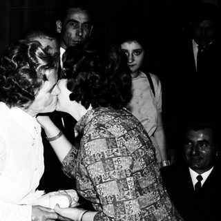 Here's a brief summary of the image: Man and woman embracing in a crowded, dimly lit setting.