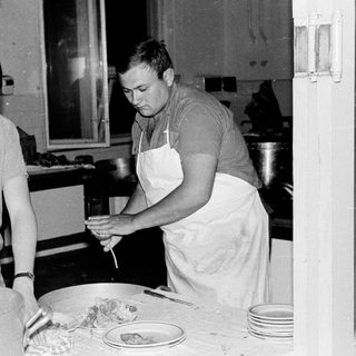 Two men work in a kitchen, possibly making cheese.