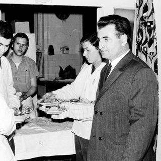 Here's a brief summary of the image: People serve food in a kitchen setting.