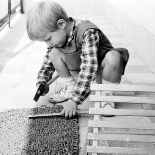 Boy uses a hammer on a wooden structure outdoors.