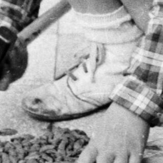 Boy uses a hammer on a wooden structure outdoors.