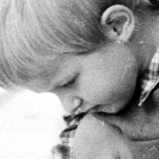 Boy uses a hammer on a wooden structure outdoors.