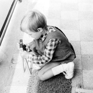 Here's a brief summary of the image: Boy kneels, holding a camera near a door.