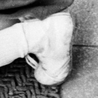 Here's a brief summary of the image: Boy kneels, holding a camera near a door.