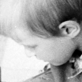 Here's a brief summary of the image: Boy kneels, holding a camera near a door.