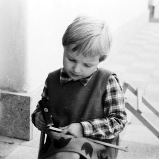 Here's a brief summary of the image: Young boy sits, focused on something in his hands.