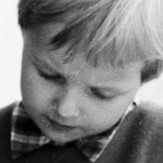 Here's a brief summary of the image: Young boy sits, focused on something in his hands.