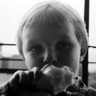 Here's a brief summary of the image: Boy eating bread, close-up, monochrome, looking directly at camera.