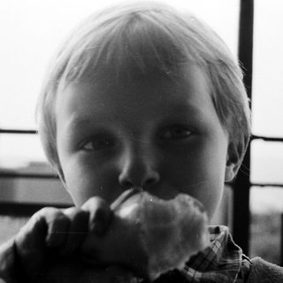 Here's a brief summary of the image: Boy eating bread, close-up, monochrome, looking directly at camera.
