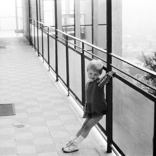 Girl stands on a balcony, looking out at a view.