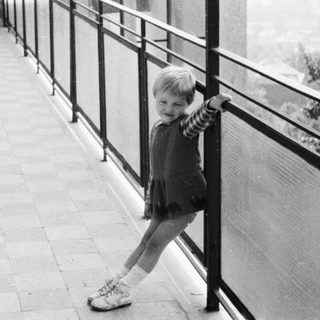 Girl stands on a balcony, looking out at a view.
