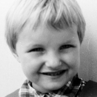 Here's a brief summary of the image: Black and white portrait of a smiling young boy.