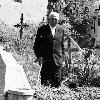 Man with cane stands in a cemetery with two women.