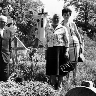 Man with cane stands in a cemetery with two women.