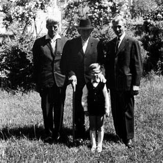 Here's a brief summary of the image: Three men and a young girl stand in a garden.