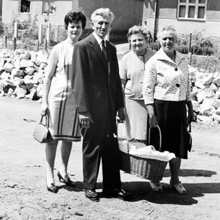 Family portrait in front of houses, carrying baskets.