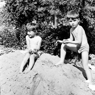 Two shirtless boys sit on a mound of dirt.