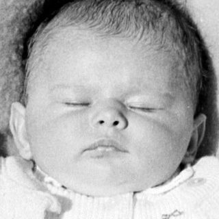 Black and white photo of a baby in a cradle.