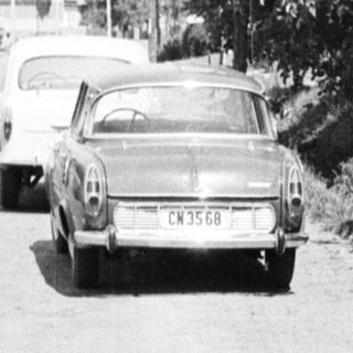 Black and white photo of three people standing near a car.