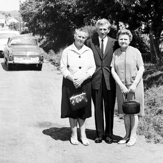 Black and white photo of three people standing near a car.