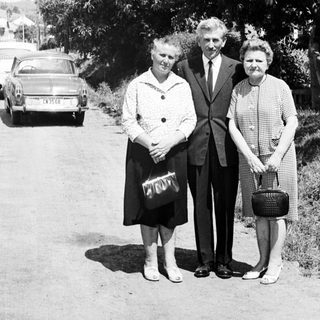 Black and white photo of three people standing near a car.