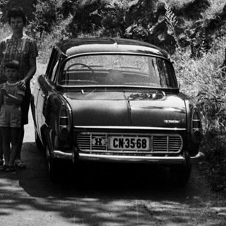 Man and child stand beside a car on a mountain road.