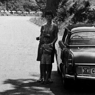Man and child stand beside a car on a mountain road.