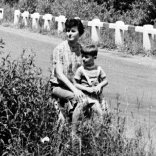 Person with child seated near a road in a wooded area.