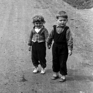 Two young boys stand on a rural, dusty road.