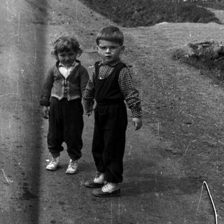 Two young boys stand on a rural, unpaved road.