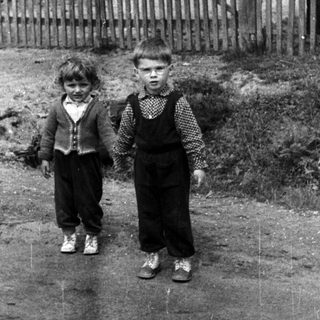Two young boys stand on a road in front of a house.