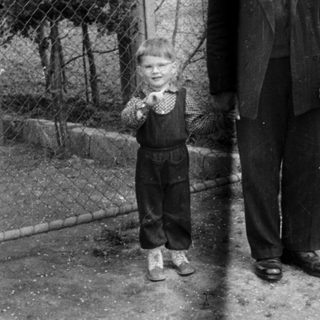 An older man stands next to a young boy outdoors.