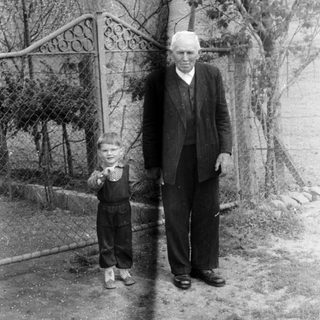An older man stands next to a young boy outdoors.