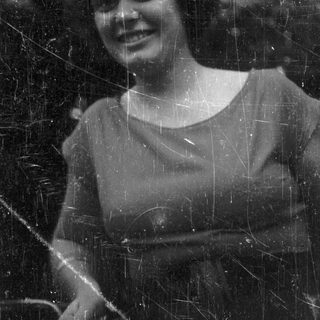 Here's a brief summary: Woman with curly hair smiles outdoors in black and white.