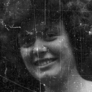 Here's a brief summary: Woman with curly hair smiles outdoors in black and white.