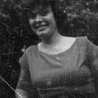 Here's a brief summary: Woman with curly hair smiles outdoors in black and white.